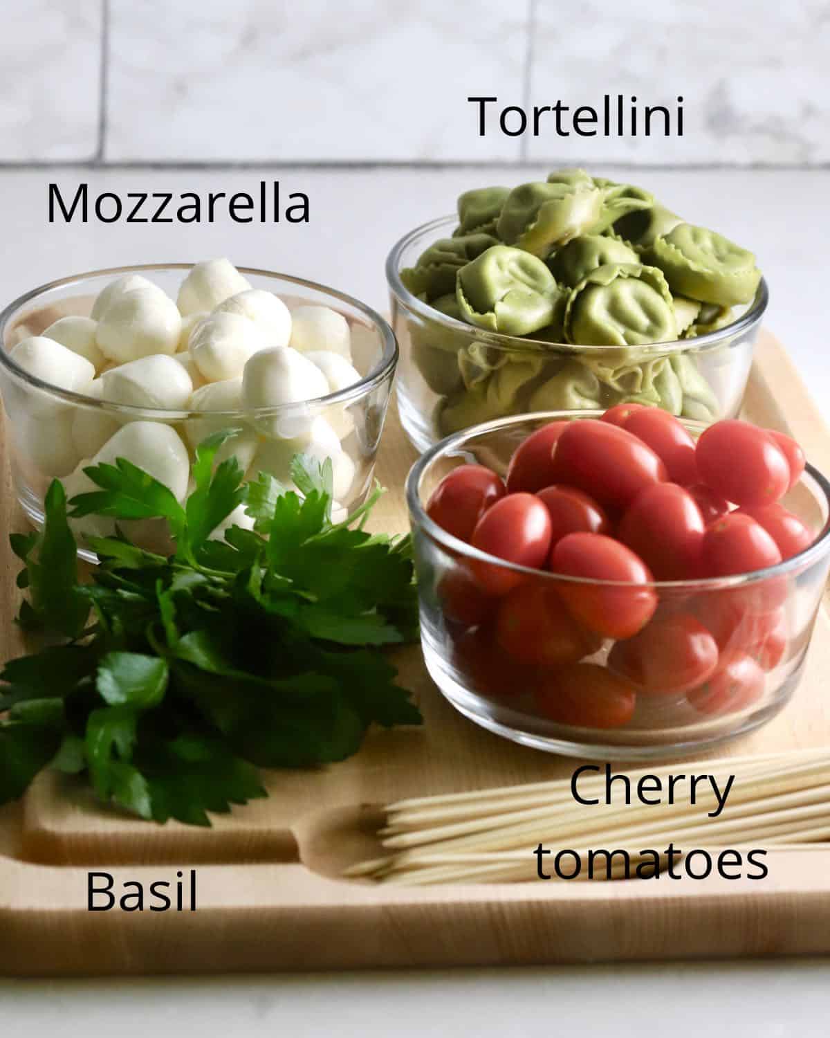 Cherry tomatoes, mozzarella,  tortellini and basil on a cutting board. 