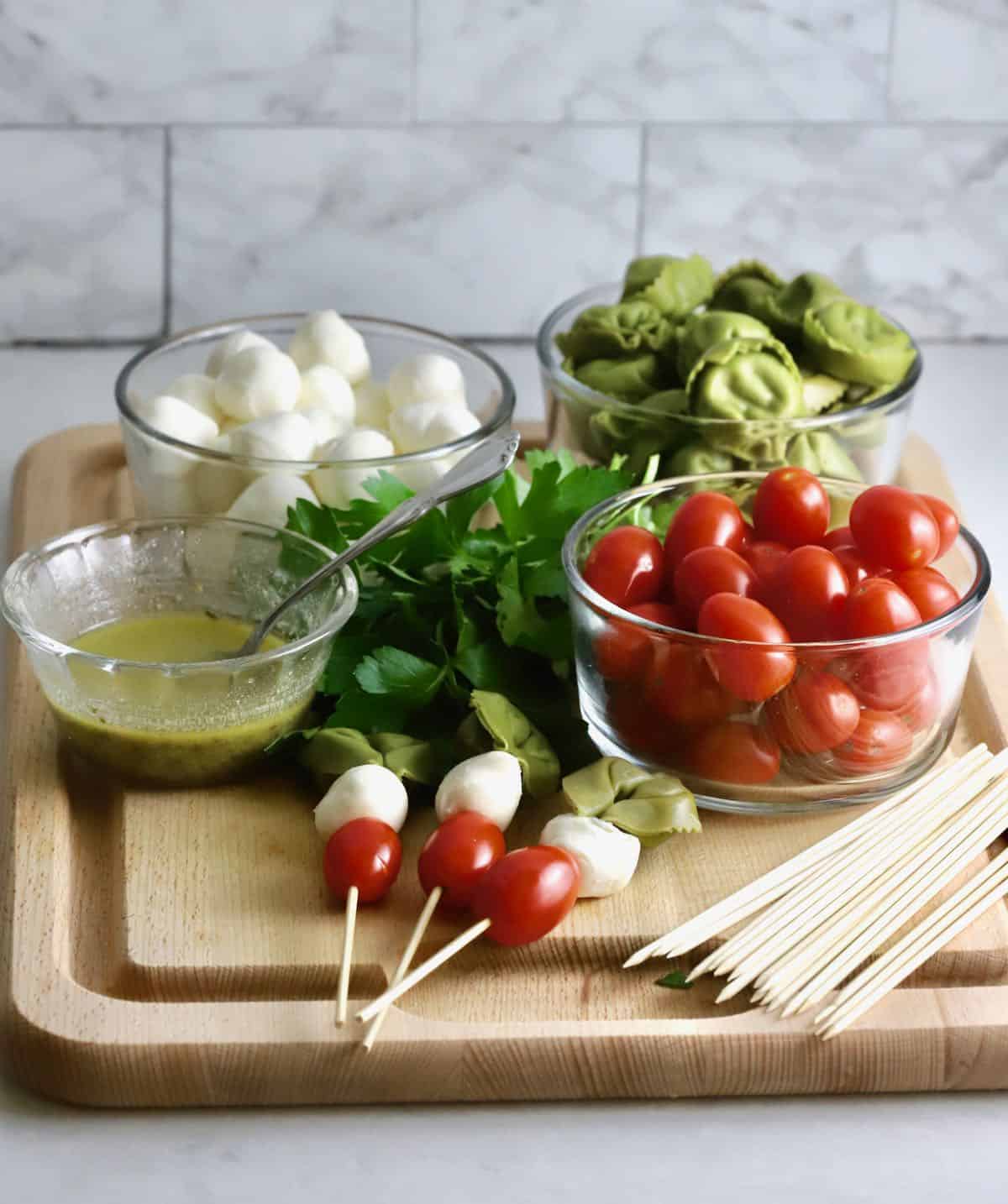 Three caprese skewers on a cutting board with a stack of skewers. 