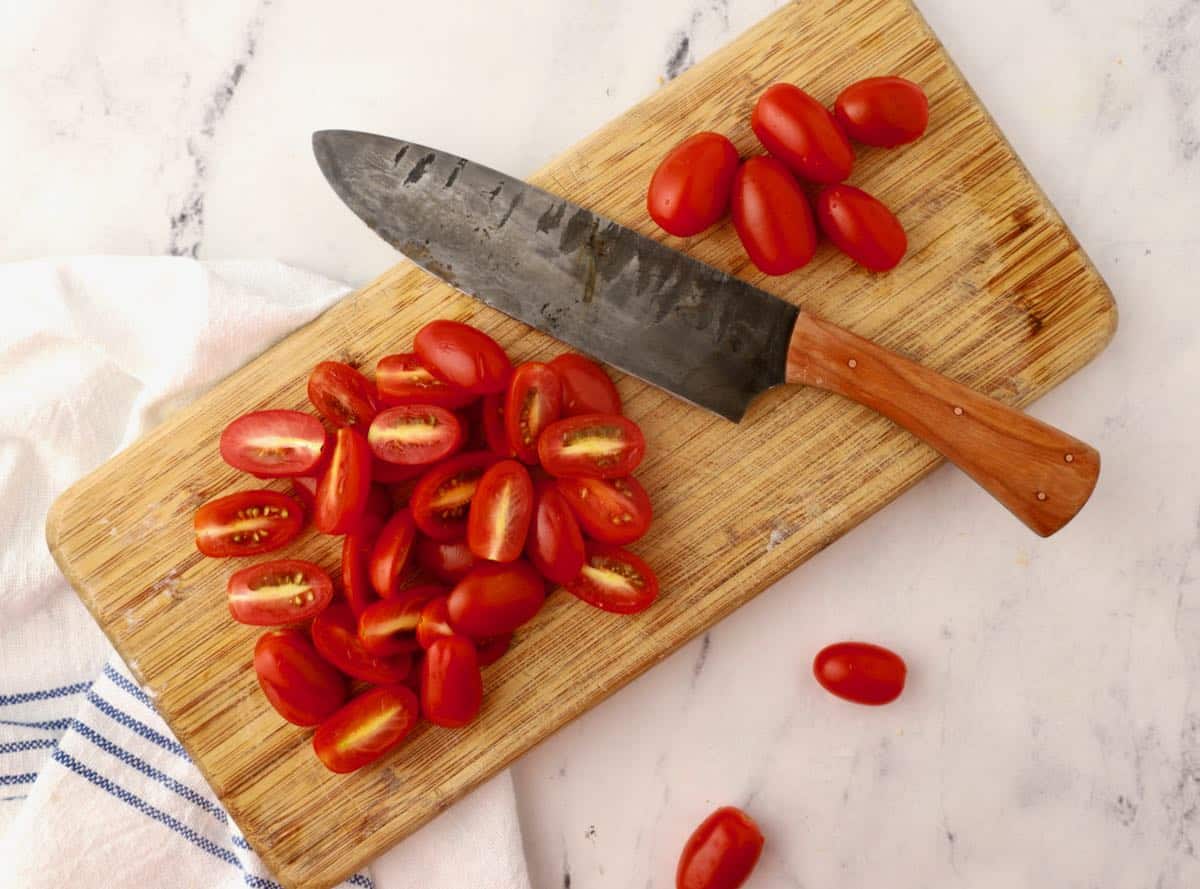 Cherry tomatoes cut in half on a cutting board. 