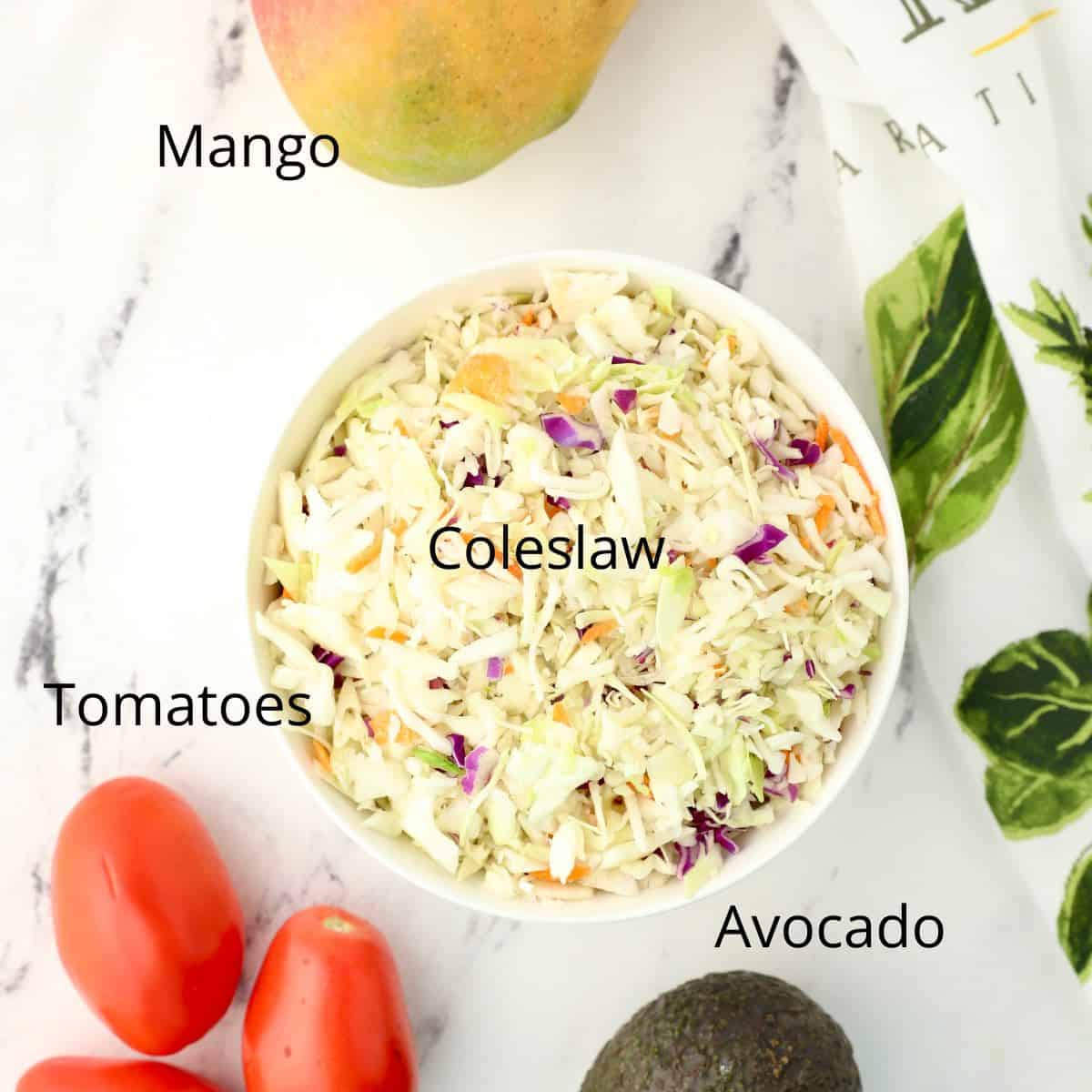 A bowl of coleslaw, tomatoes and mango. 