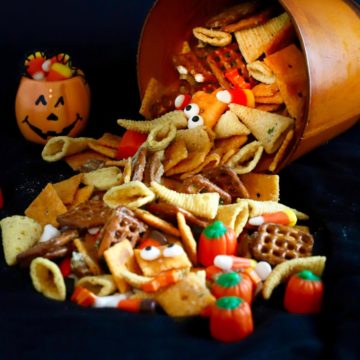 Bugles, candy corn, pretzels and nuts spilling out oof a orange bucket.