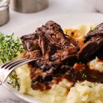 Oven baked short ribs on a plate of mashed potatoes.