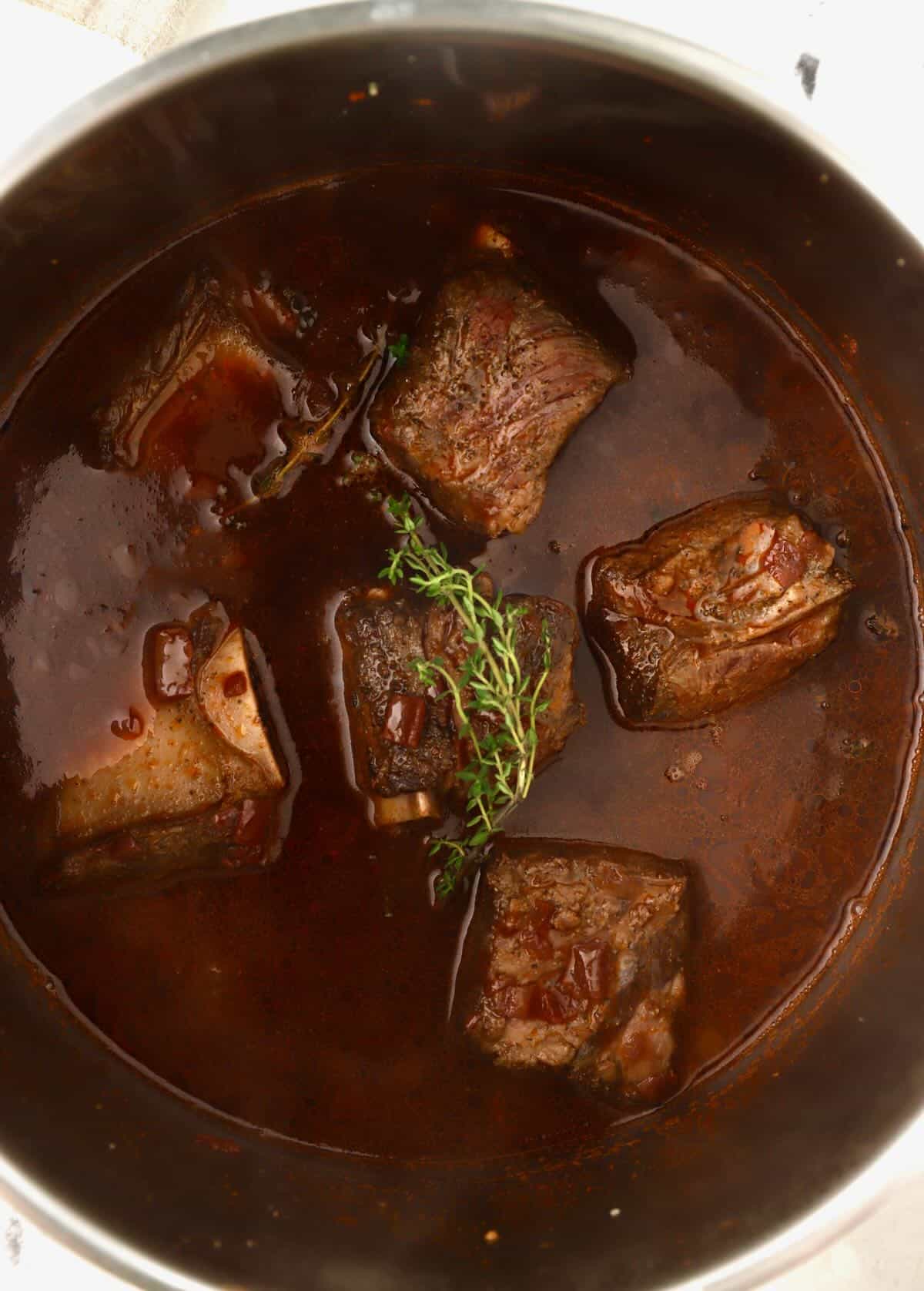 Beef short ribs cooking in a red wine sauce. 