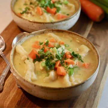 Two bowls of chicken and dumplings topped with celery and carrots.