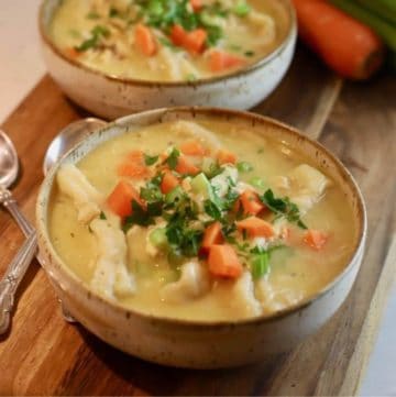 Two bowls of chicken and dumplings topped with celery and carrots.