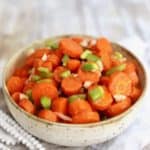 A bowl of cooked sliced carrots topped with chopped bell pepper.