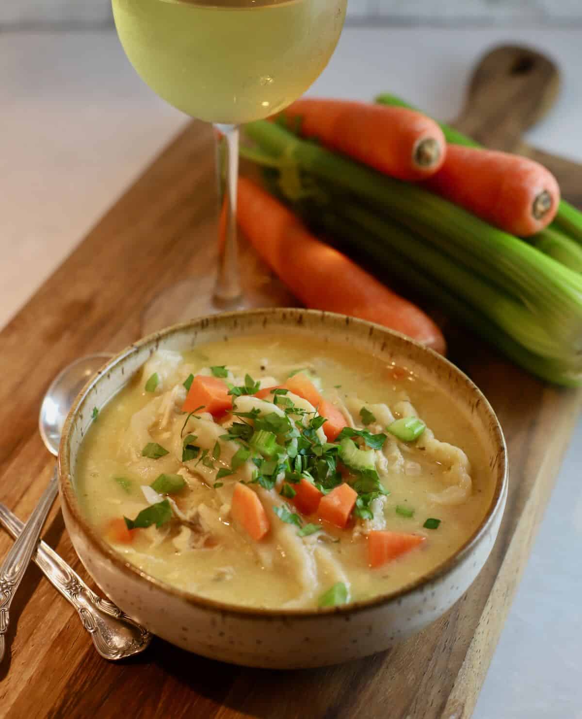 A bowl of chicken and dumplings and a glass of wine. 