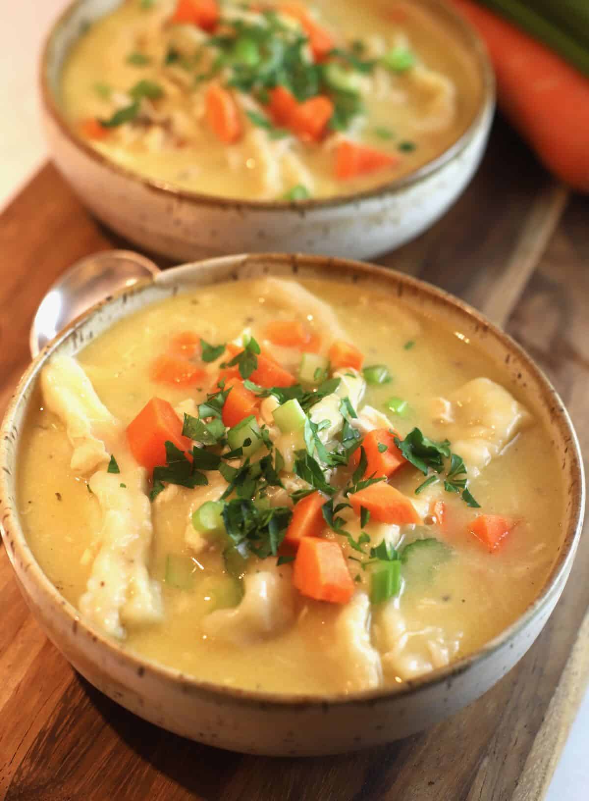 Two bowls of chicken and dumplings on a cutting board.