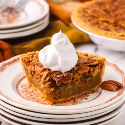 A slice of pecan pie on a plate topped with whipped cream.