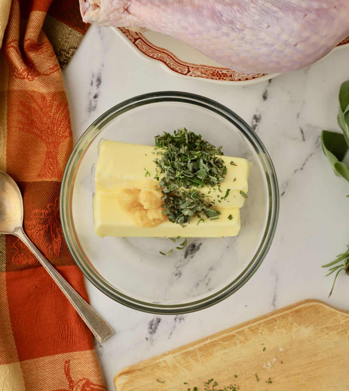 Two sticks of butter in a bowl along with herbs and garlic. 