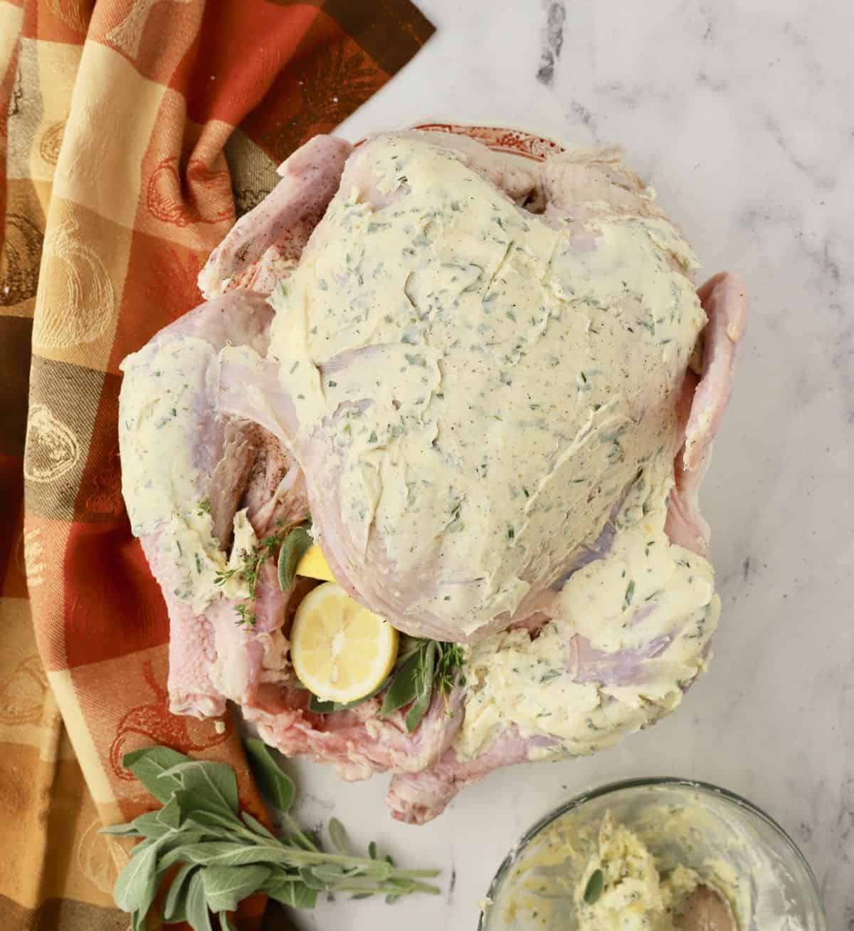 A raw turkey covered with a herb and garlic butter rub. 