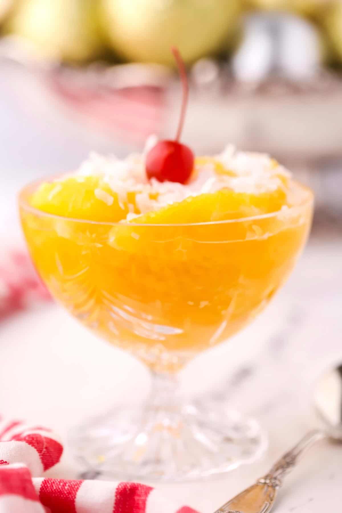 A glass serving bowl full of orange segments, topped with a cherry. 