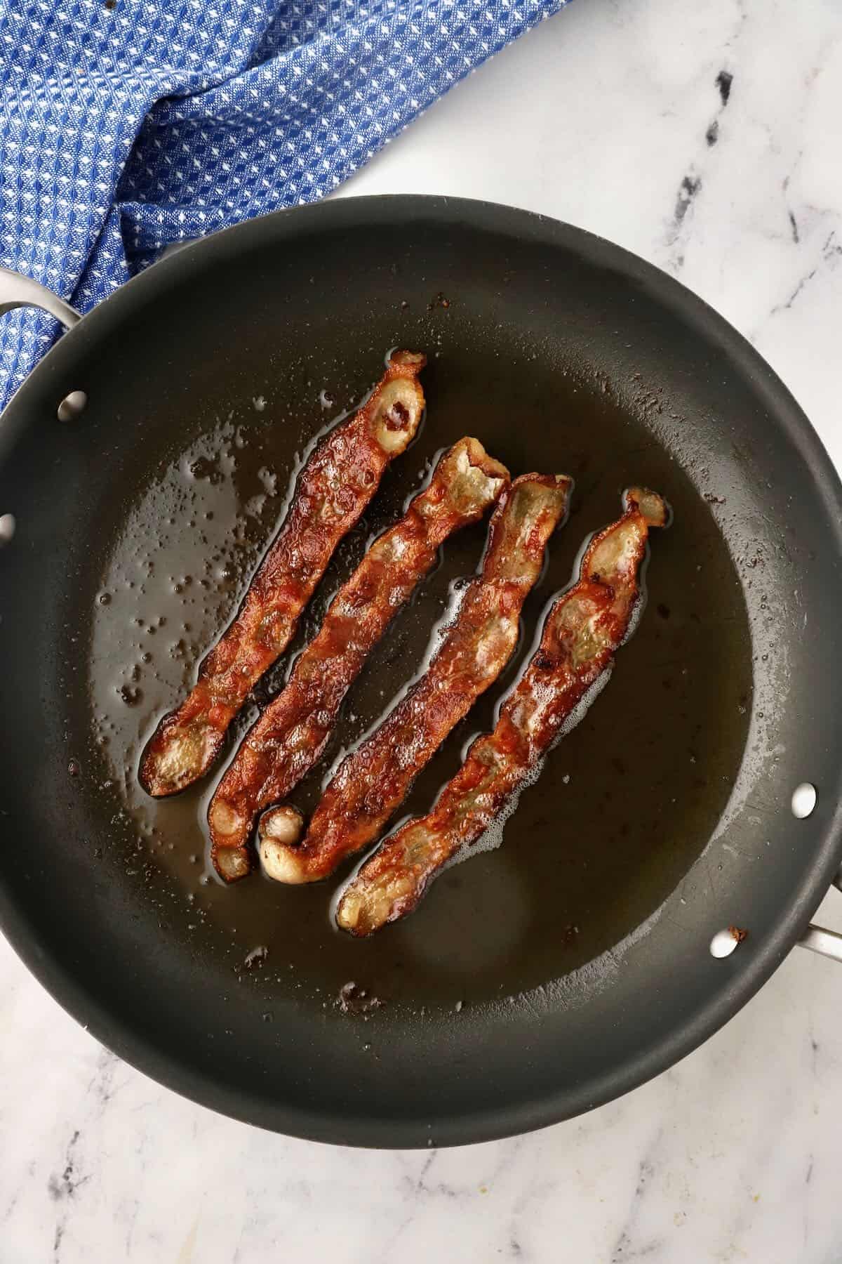 Four slices of bacon cooking in a skillet. 