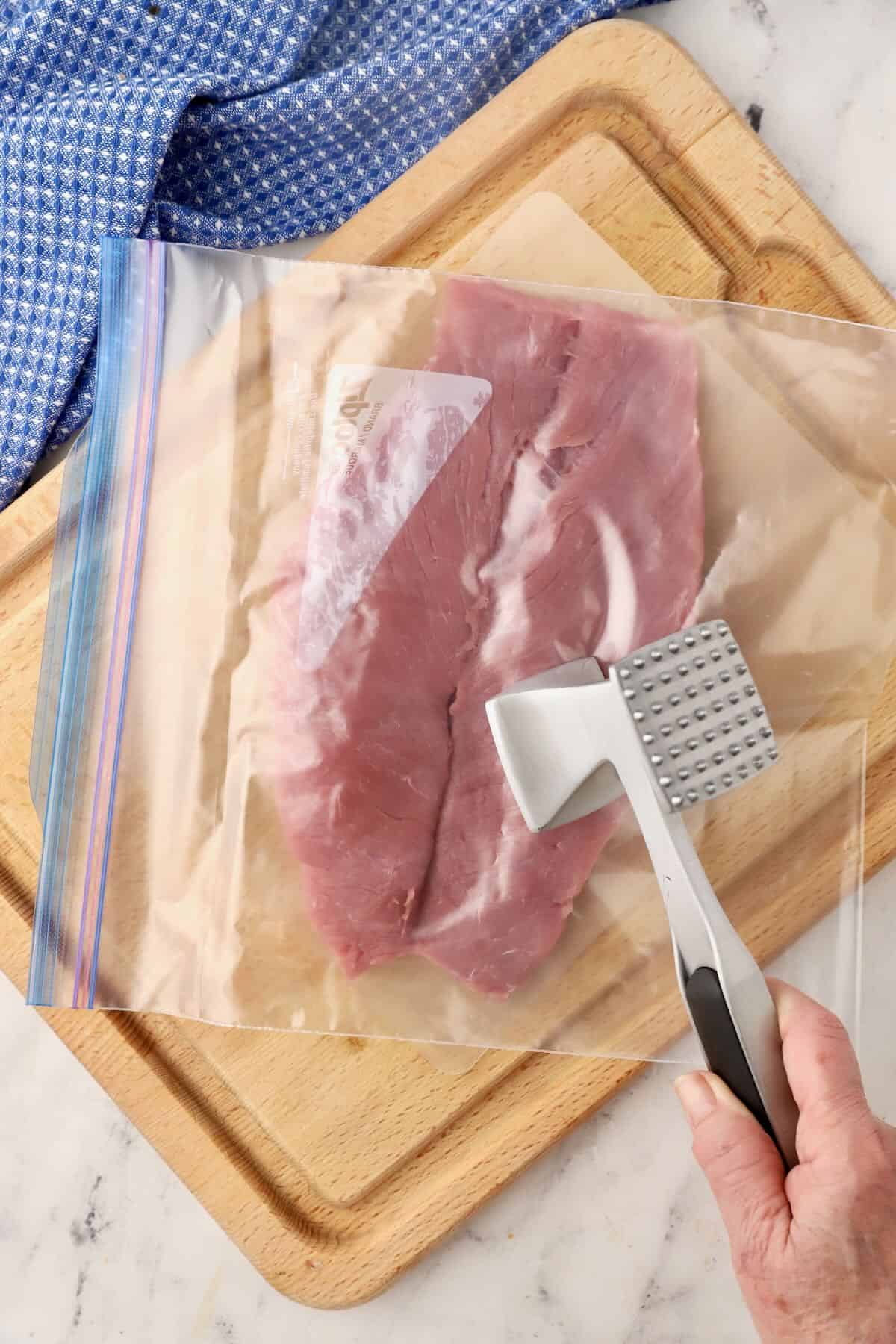 A butterflied pork tenderloin with a zip lock bag over it. 