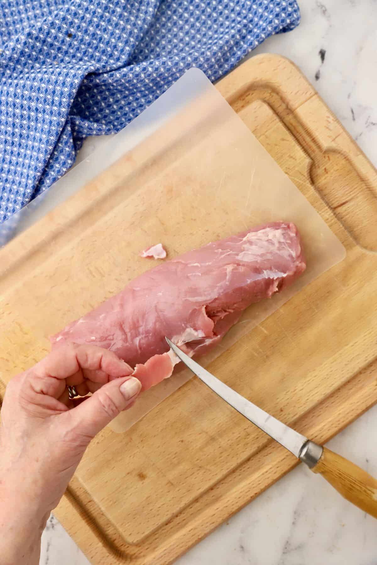 Using a knife to remove silver skin from a pork tenderloin. 