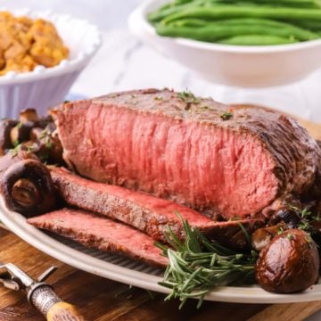 A New York Strip Roast with slices cut with a bowl of green beans behind it.