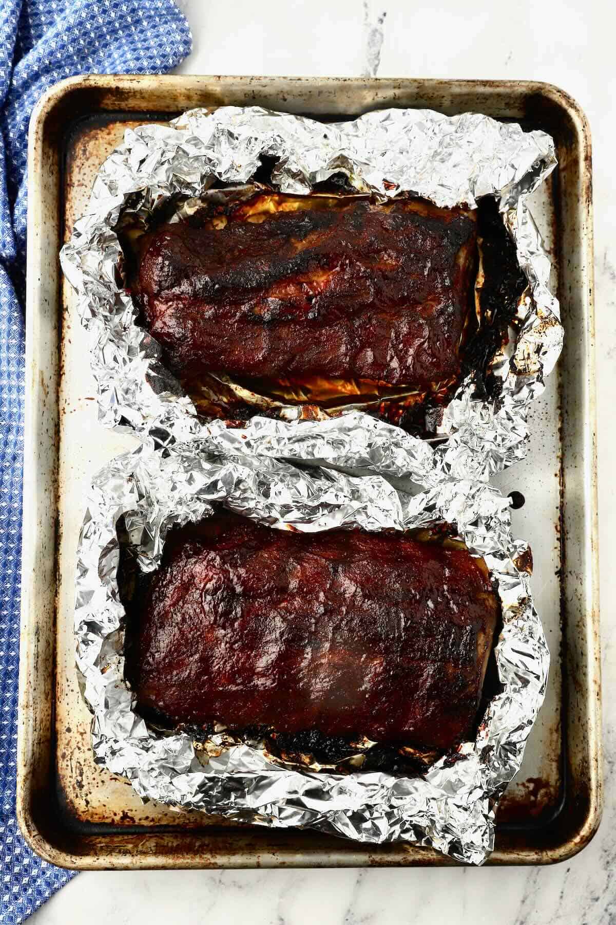 Two oven-baked racks of ribs on a baking sheet. 