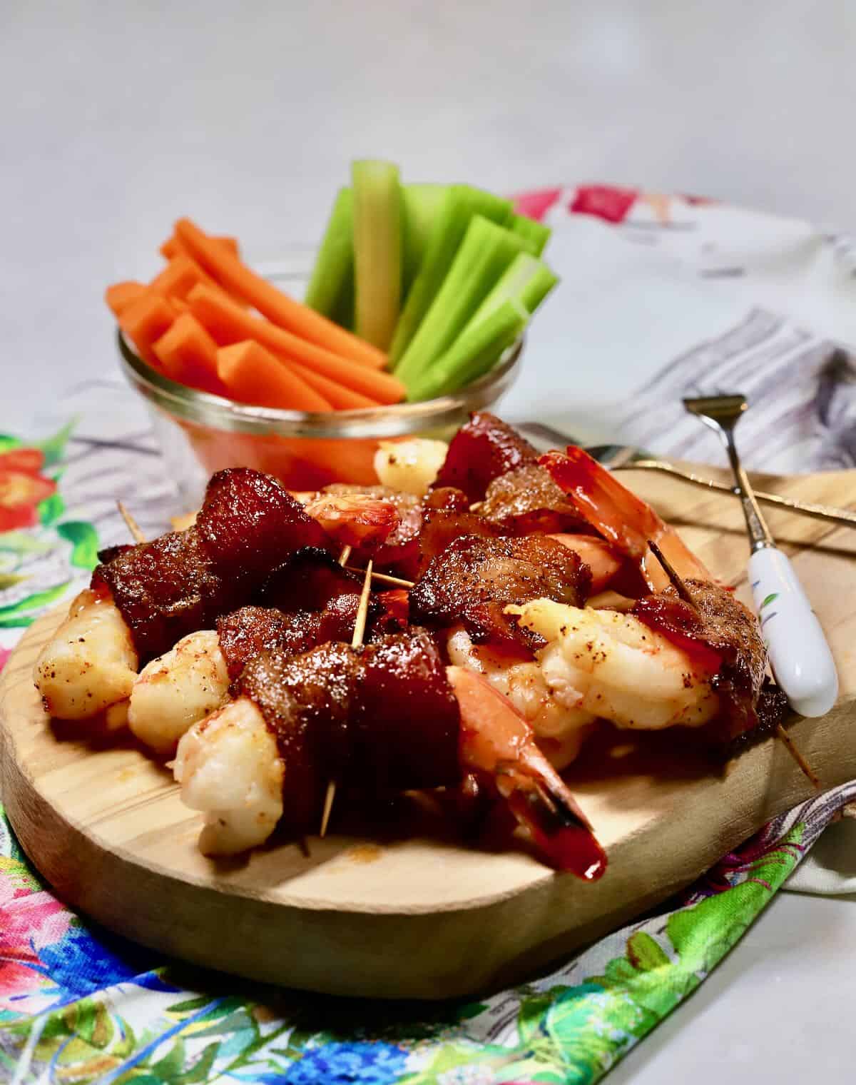 Bacon wrapped shrimp on a cutting board with carrot sticks and celery. .