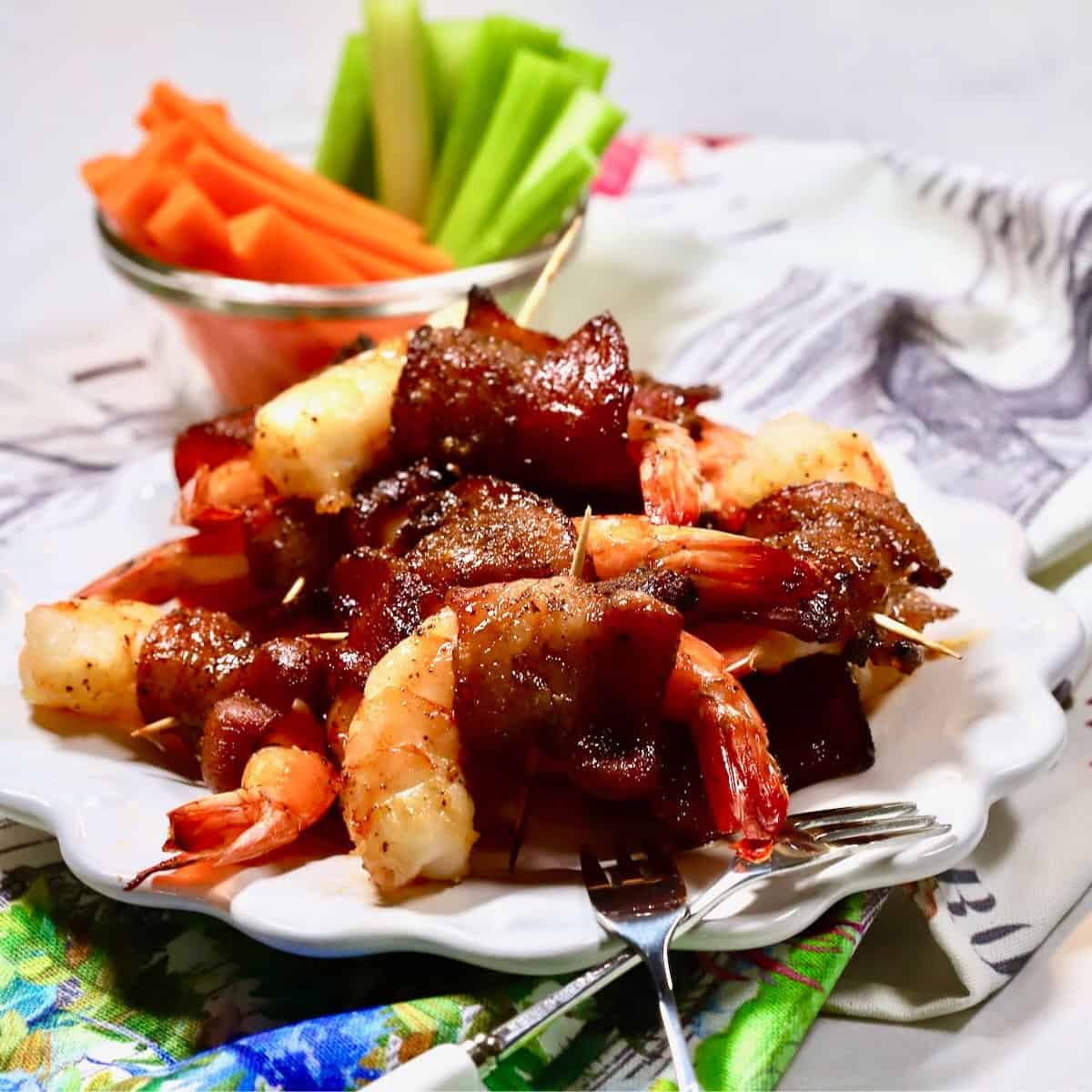 Bacon wrapped shrimp on a white plate with carrots and celery.