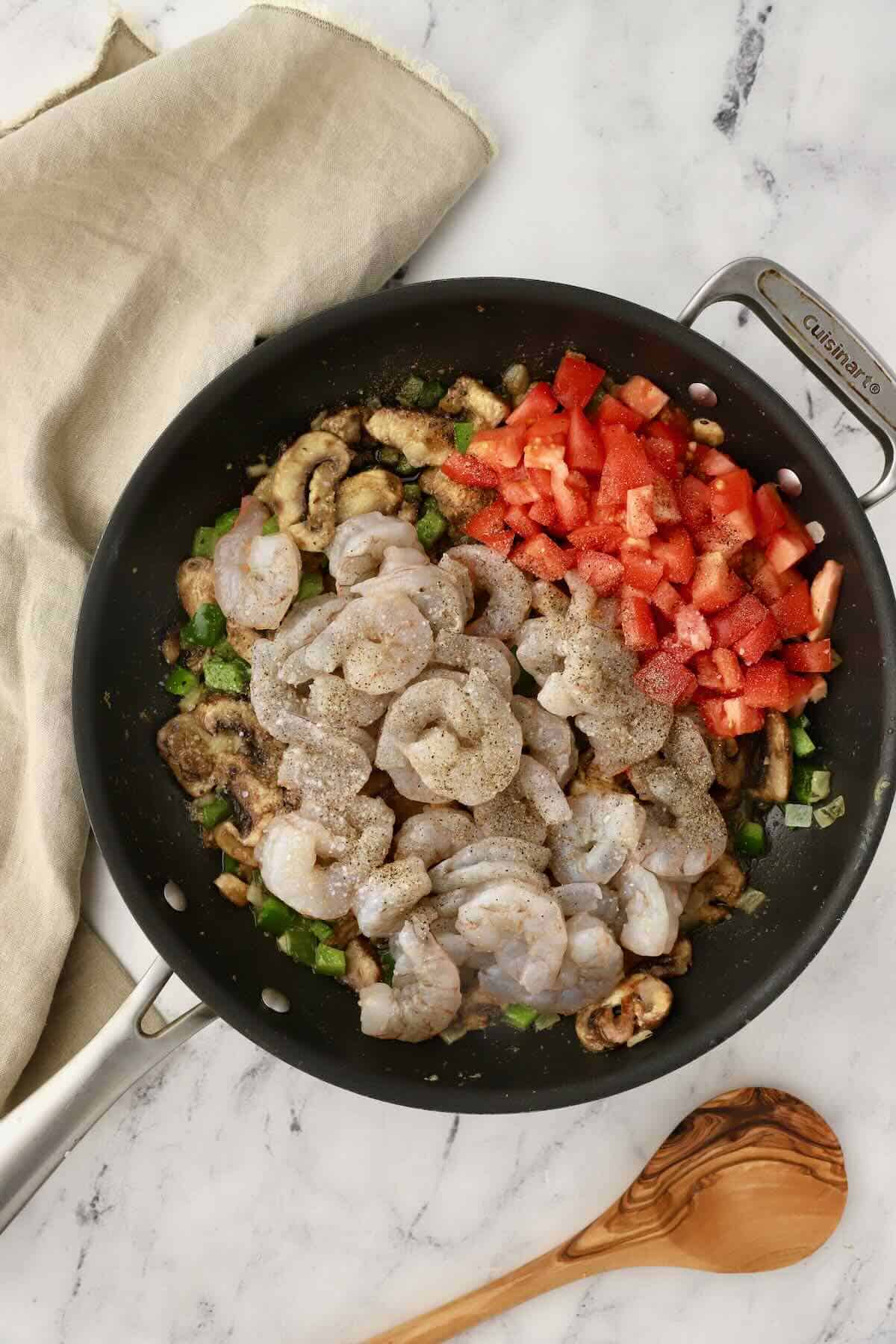 Raw shrimp and chopped tomatoes in a skillet.