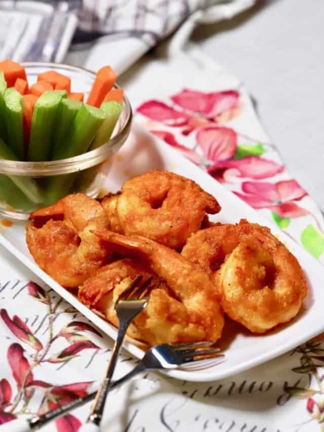 Buffalo shrimp on a white plate with celery and carrots. 
