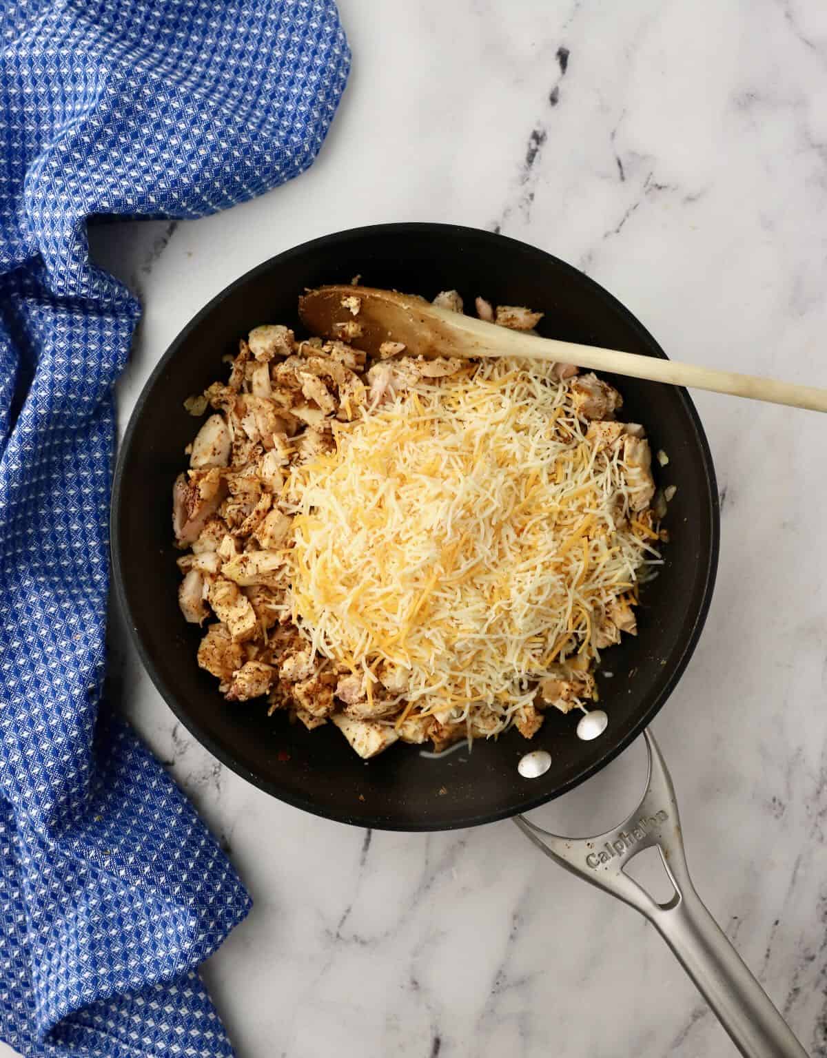 Chopped chicken topped with shredded cheese in a skillet. 