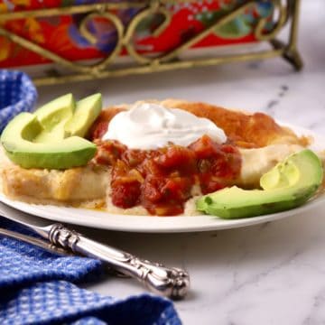 A serving of Sour Cream Chicken Enchilada Casserole on a white plate, garnished with avocado slices.
