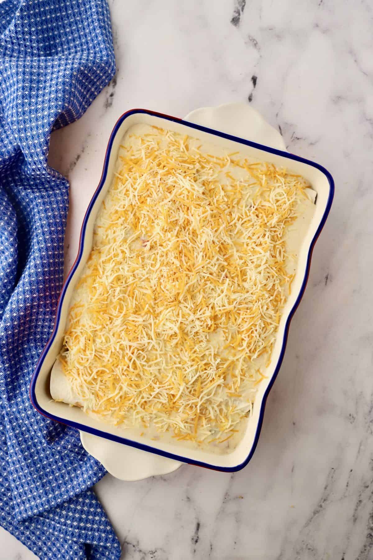 A baking dish full of chicken tortillas and topped with shredded cheese. 
