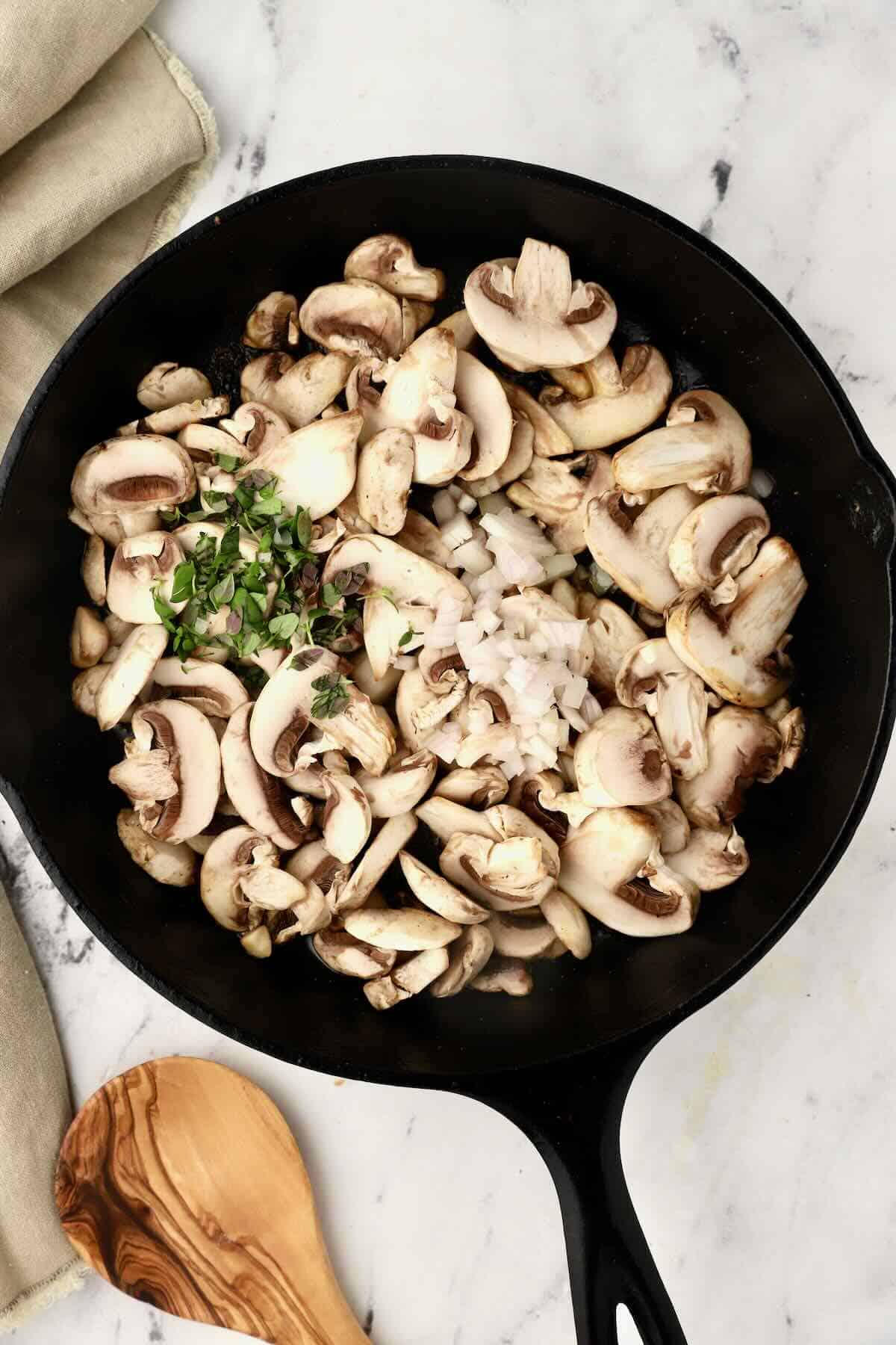 Sliced mushrooms cooking in a cast iron skillet. 