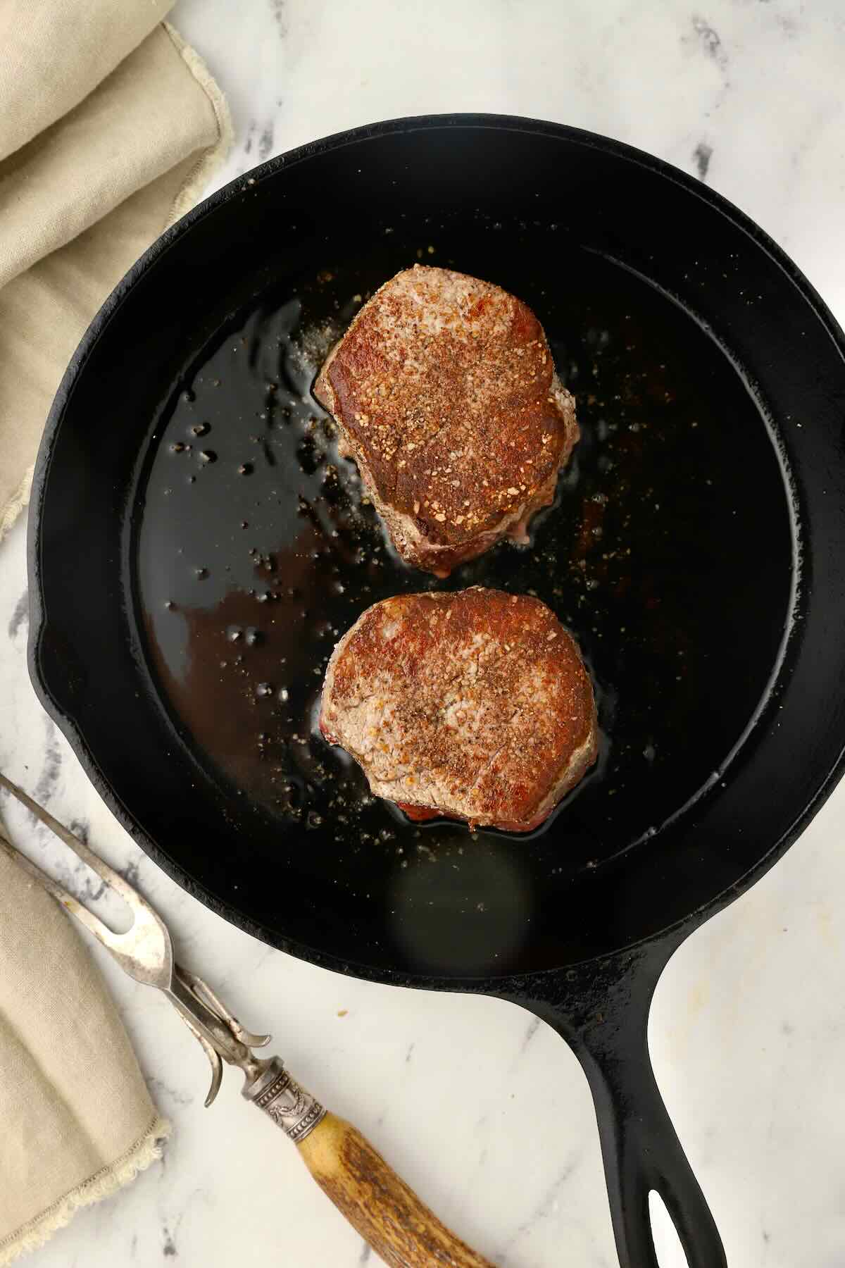 Two steaks cooking in a cast iron skillet. 