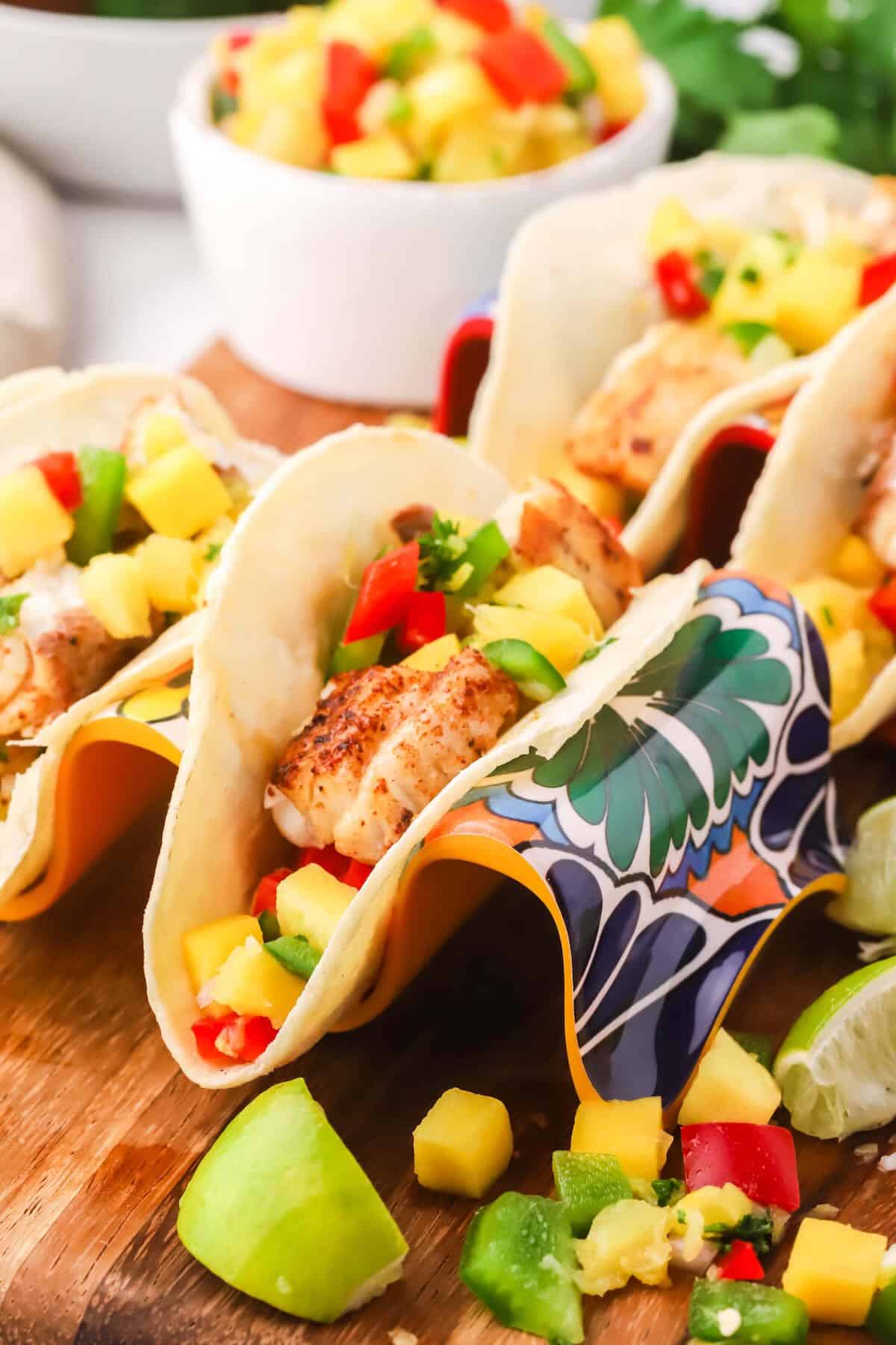 Fish tacos topped with mango salsa in taco holders. 