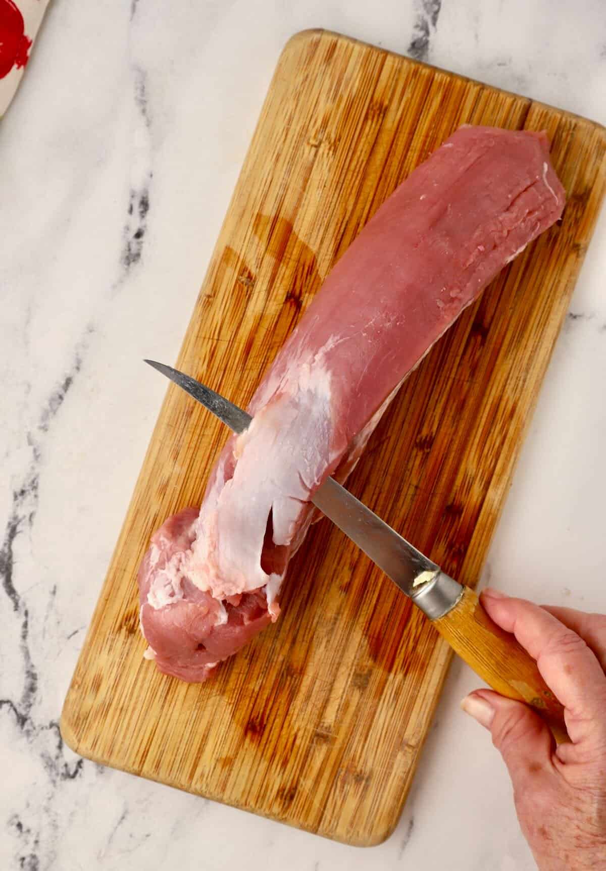 Removing silver skin with a knife on a pork tenderloin. 