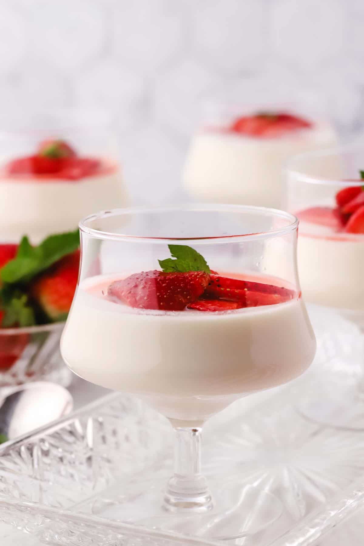 A clear glass dish full of panna cotta and sliced strawberries.