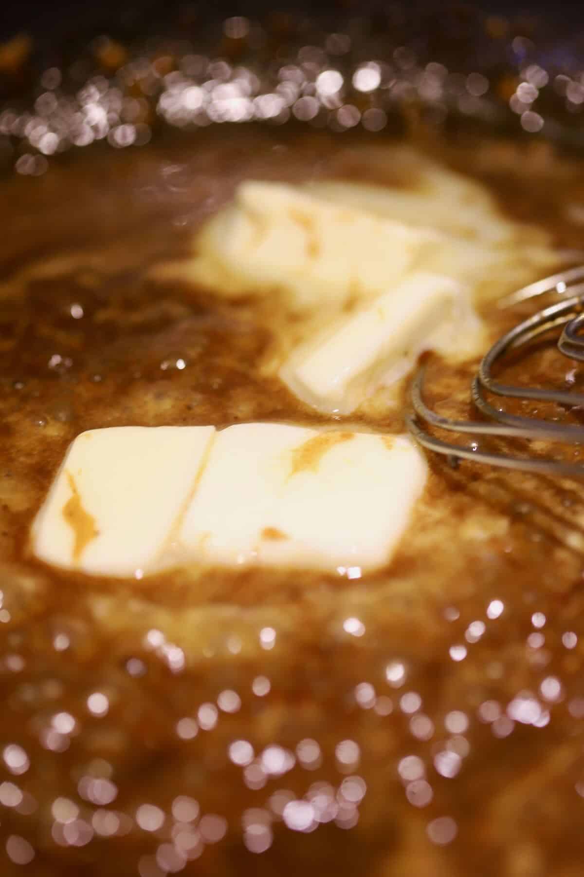 Butter being whisked into a BBQ sauce in a skillet. 