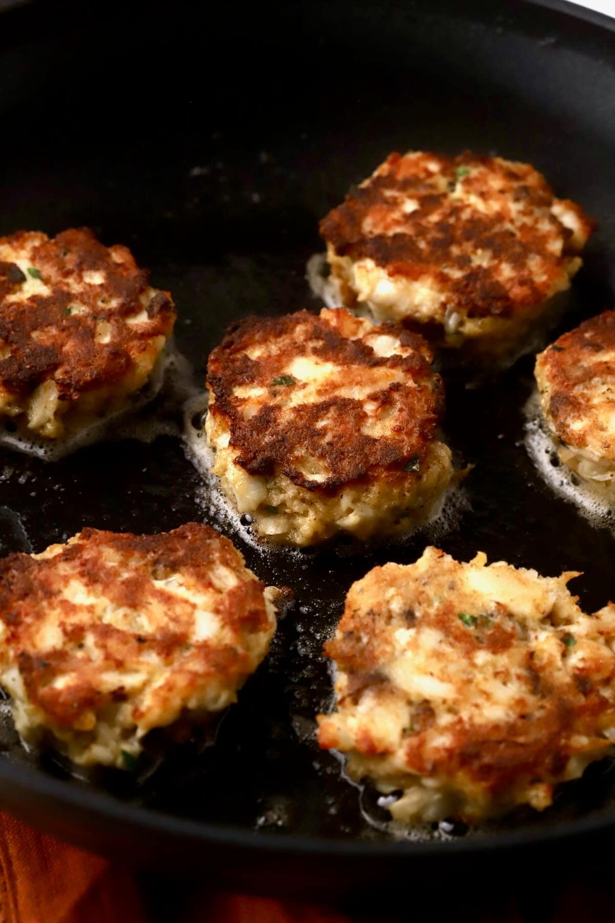 Fish cakes being pan-fried in a skillet. 