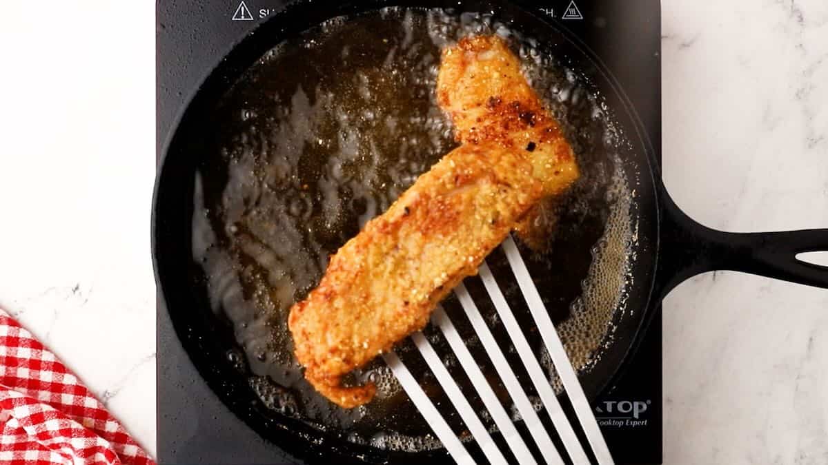 Using a fish spatula to remove fried fish from a cast iron skillet. 