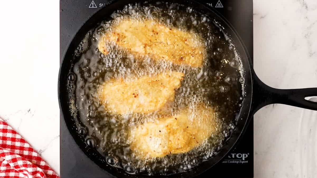 Three grouper fillets frying in a cast-iron skillet.