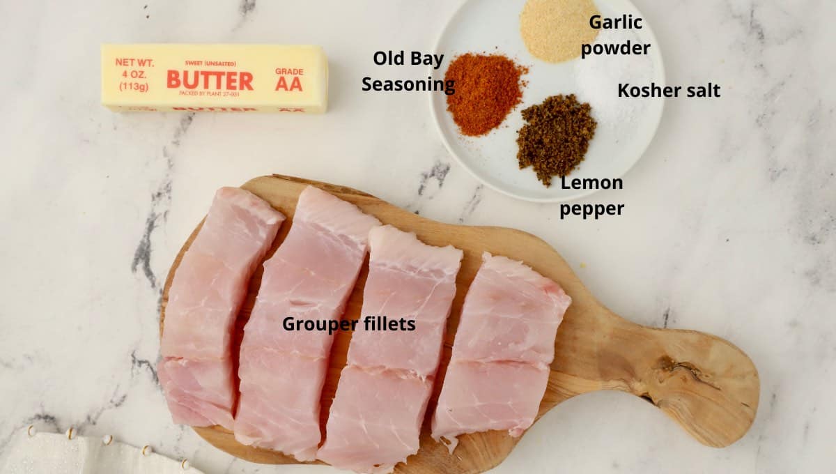 Grouper fillets on a cutting board with seasonings and a stick of butter. 
