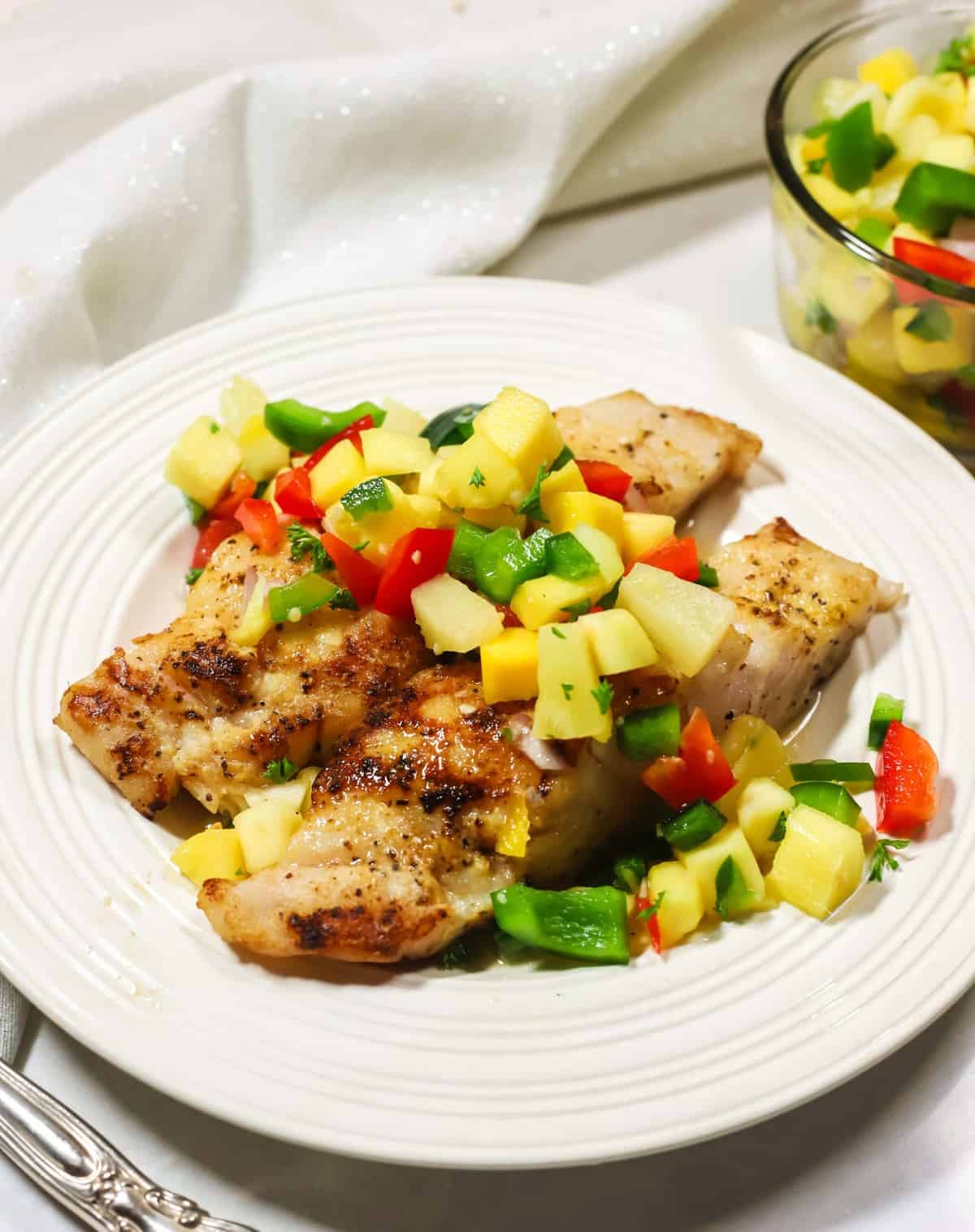 Two grilled grouper fillets on a white plate topped with mango salsa.