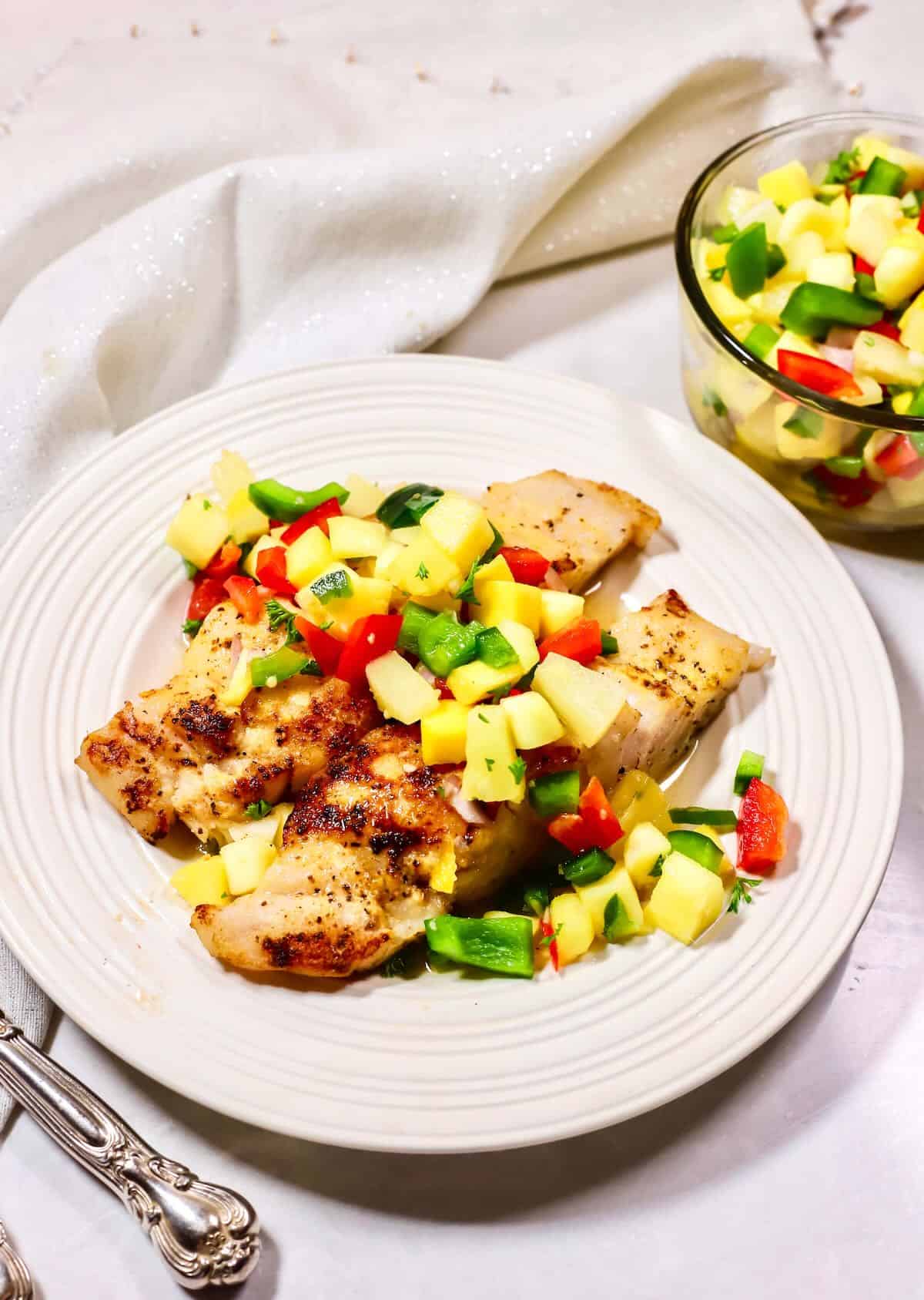 Grilled grouper on a white plate topped with mango salsa