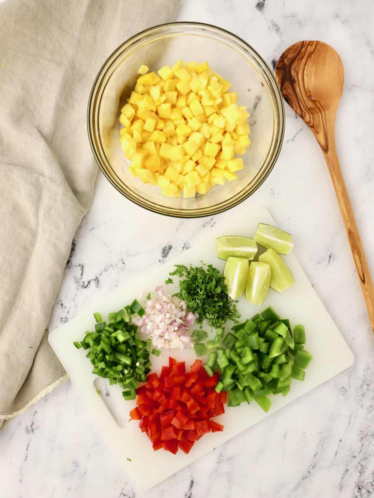 Chopped mango in a bowl with other chopped vegetables on a cutting board. 