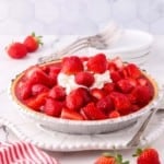 Fresh strawberry pie topped with whipped cream on a white plate.
