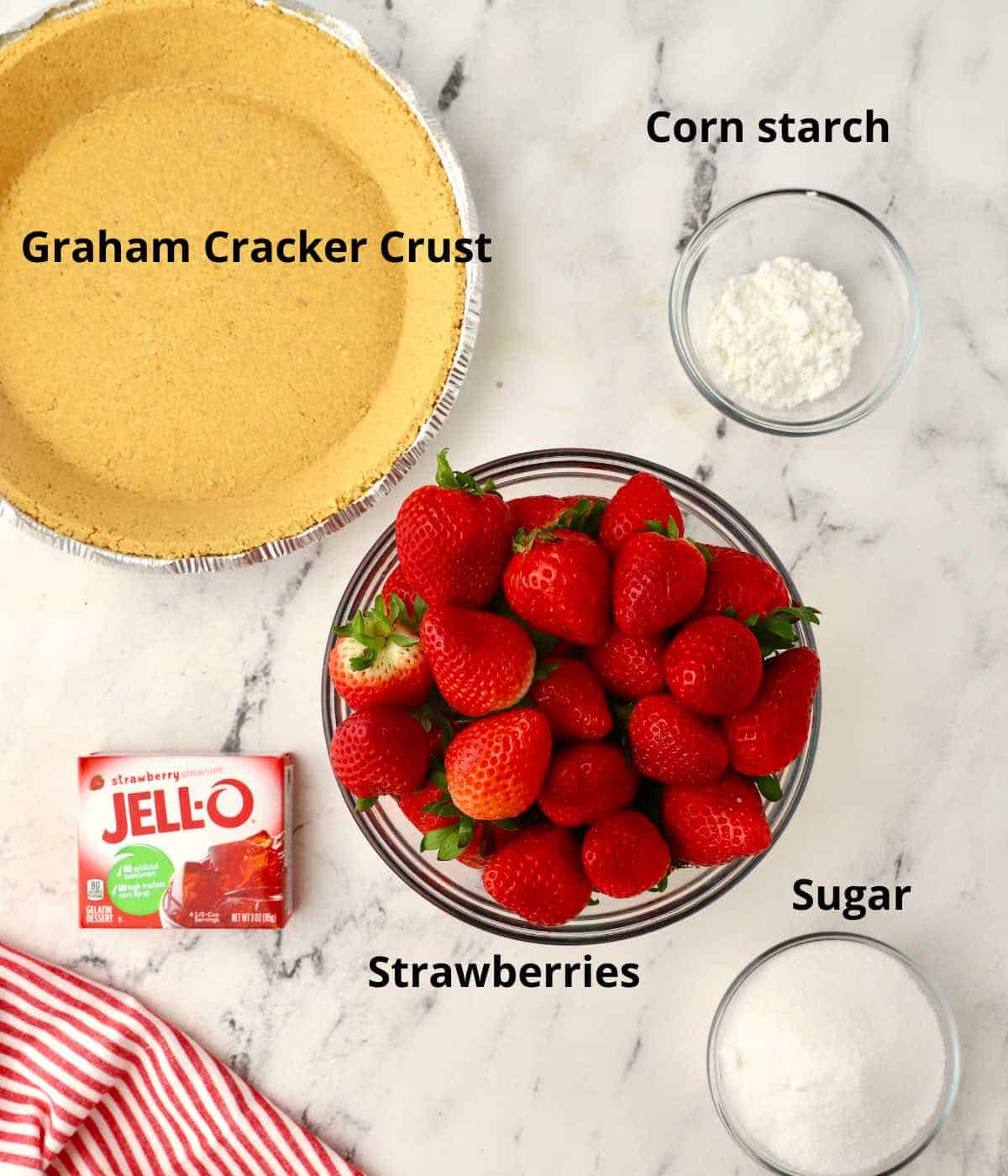 Ingredients for strawberry pie including strawberries and a graham cracker crust. 
