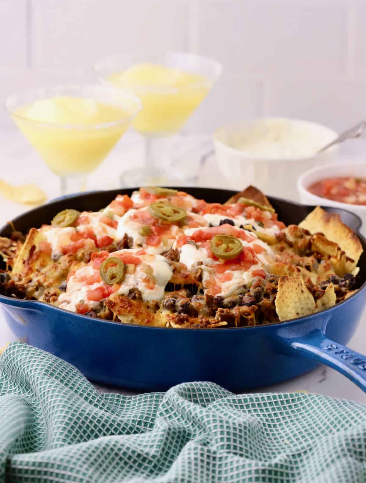 A cast iron skillet full of nachos topped with sour cream and salsa. 