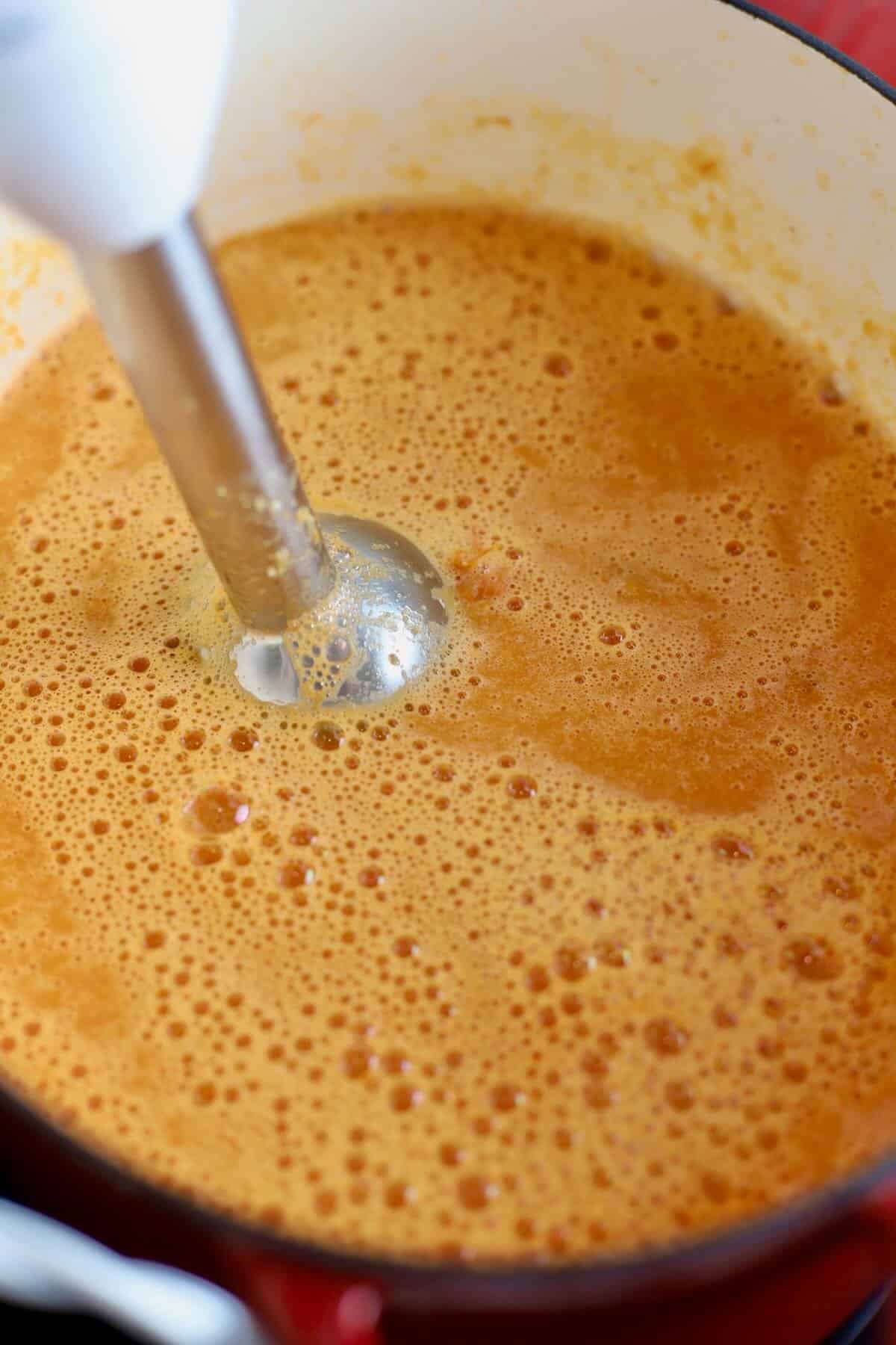 Using an immersion blender to blend up tomato soup. 