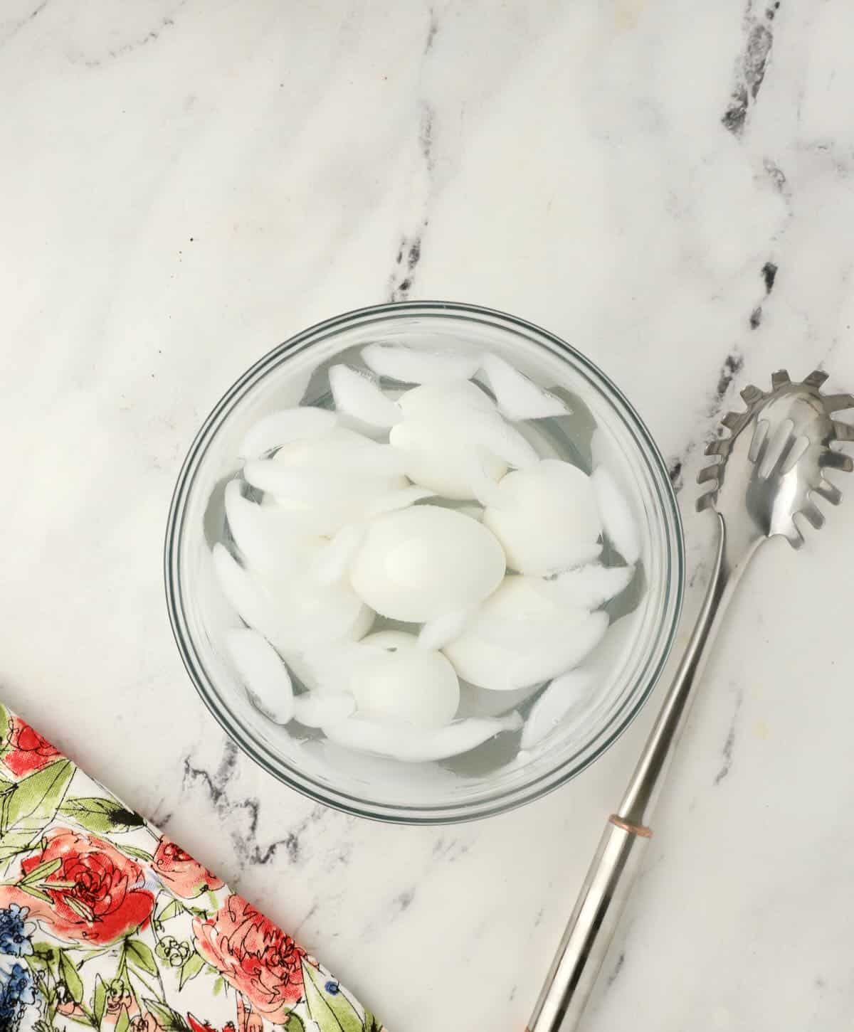 Hard boiled eggs cooling in a bowl of water and ice.