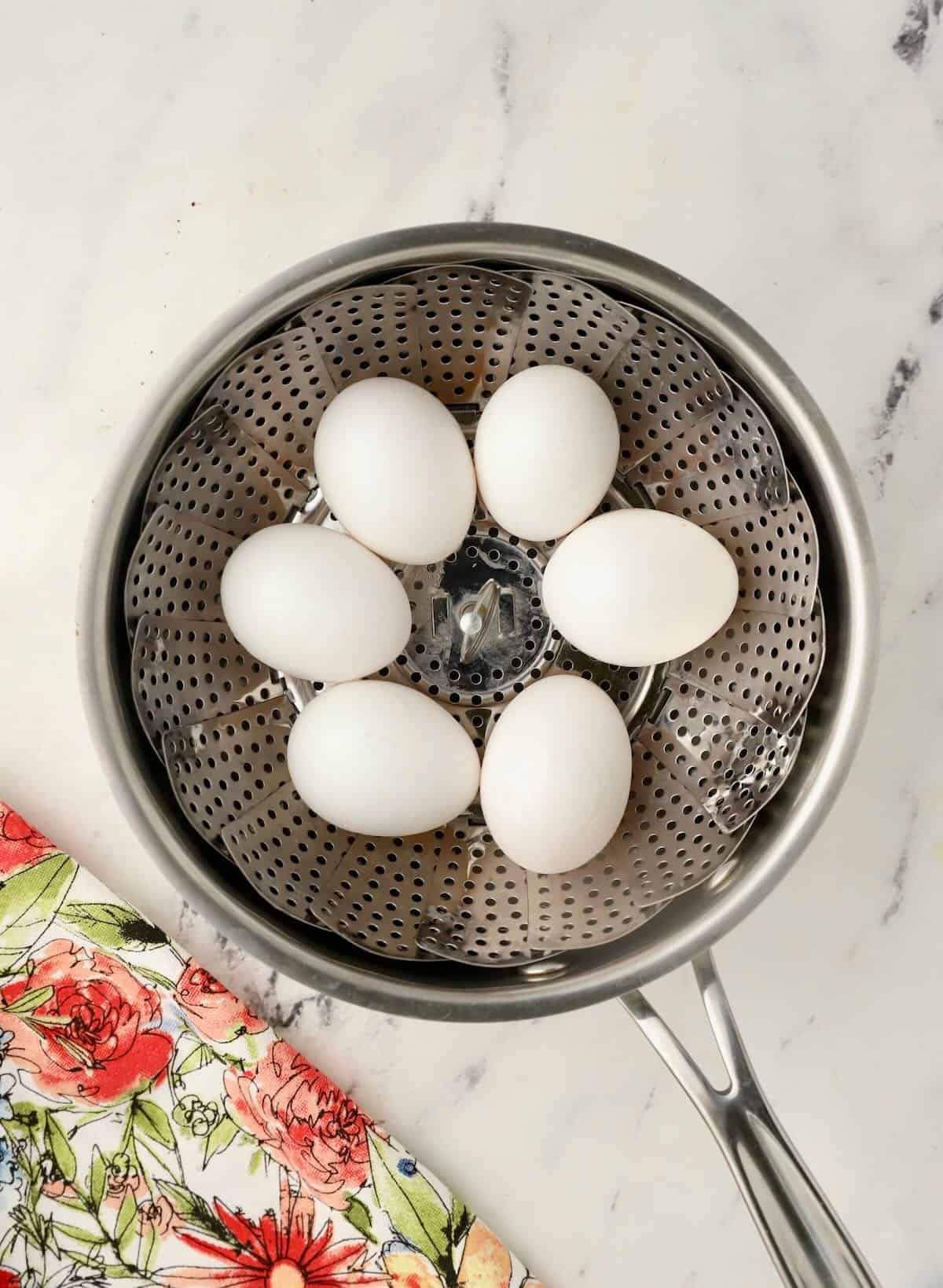 Eggs in a steamer basket in a saucepan. 