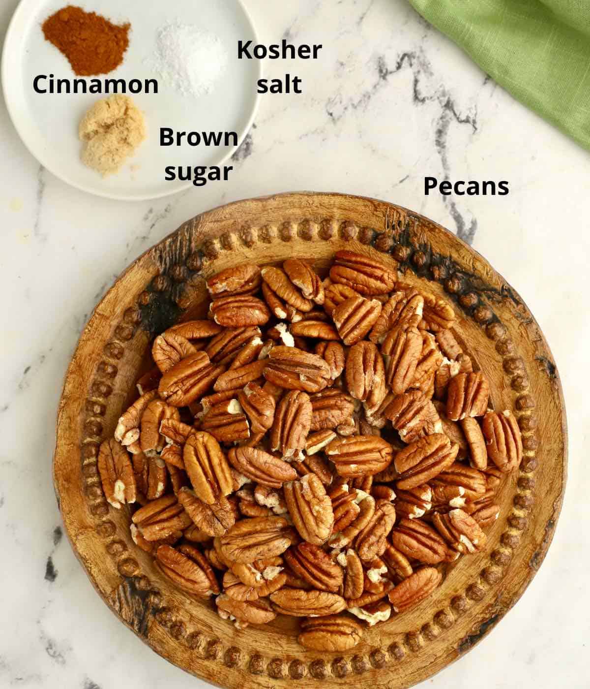 Raw pecans on a wooden plate, plus salt and cinnamon on a smaller plate. 