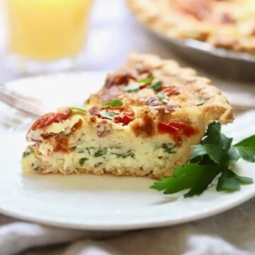 A slice of quiche with tomatoes on a white plate, garnished with a sprig of parsley.