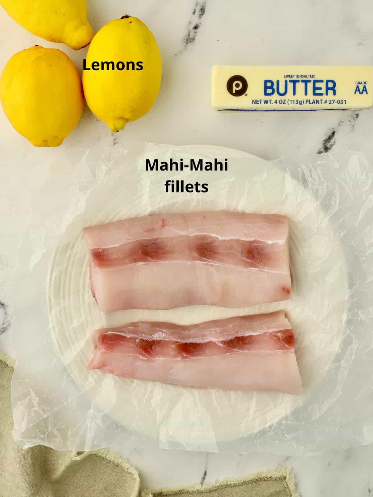 Two mahi-mahi fillets along with a stick of butter and lemons. 